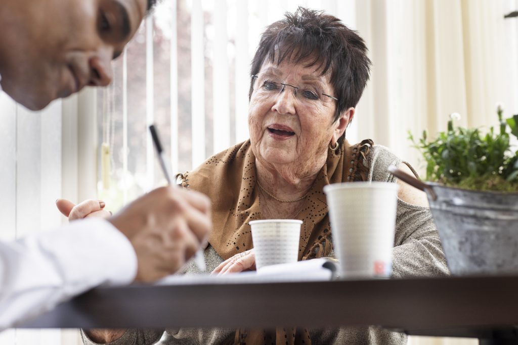 Oudere vrouw aan tafel met een man die wat opschrijft