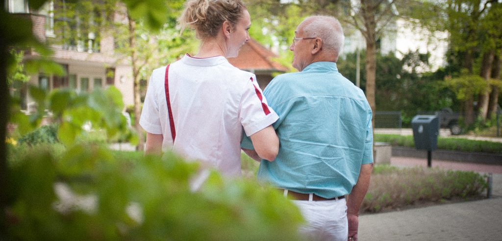 Verpleegkundige en oudere wandelen buiten